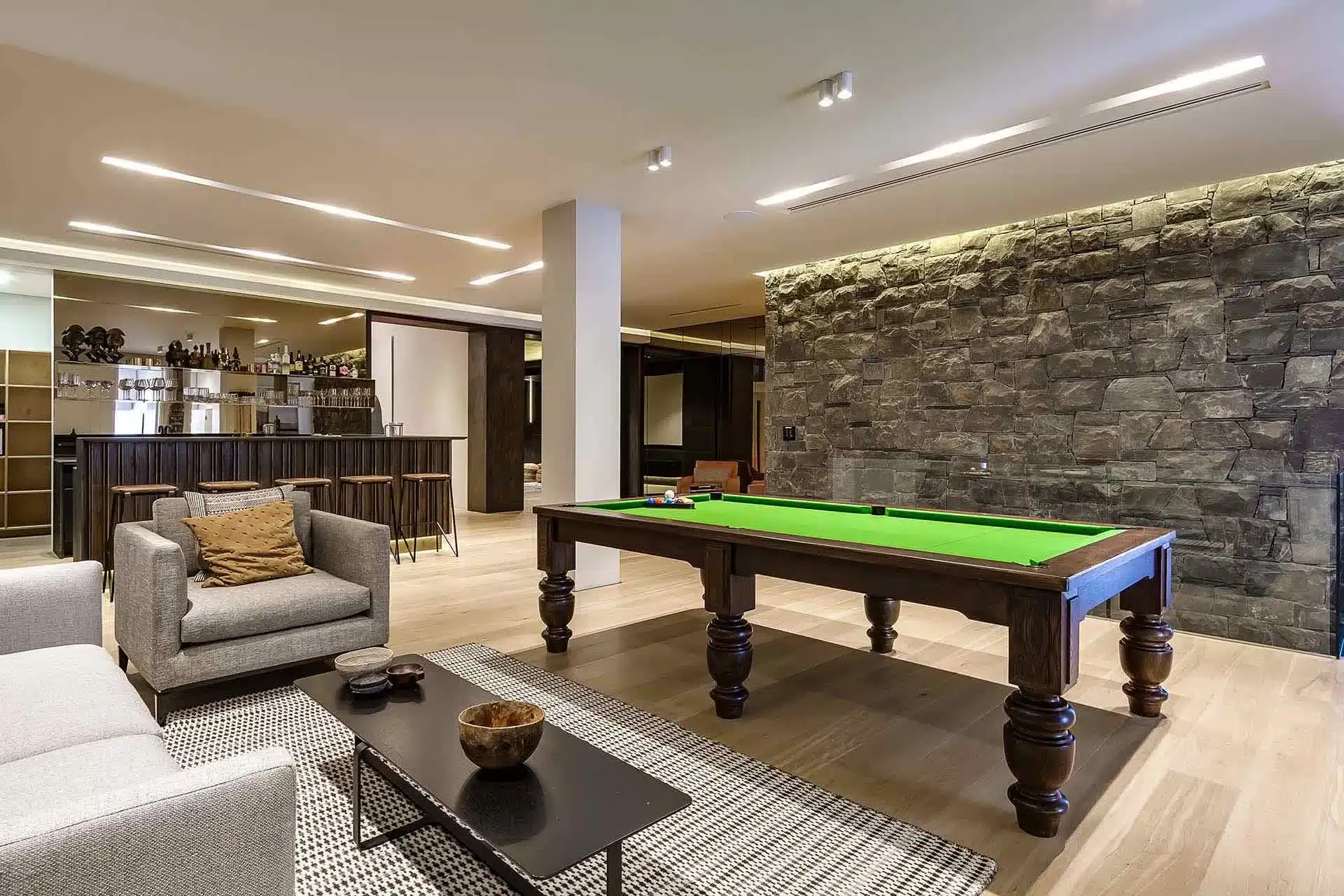 Modern lounge in a luxury villa rental with a green pool table, stone accent wall, bar area, and cozy lighting—perfect for relaxing after exploring with concierge travel services.