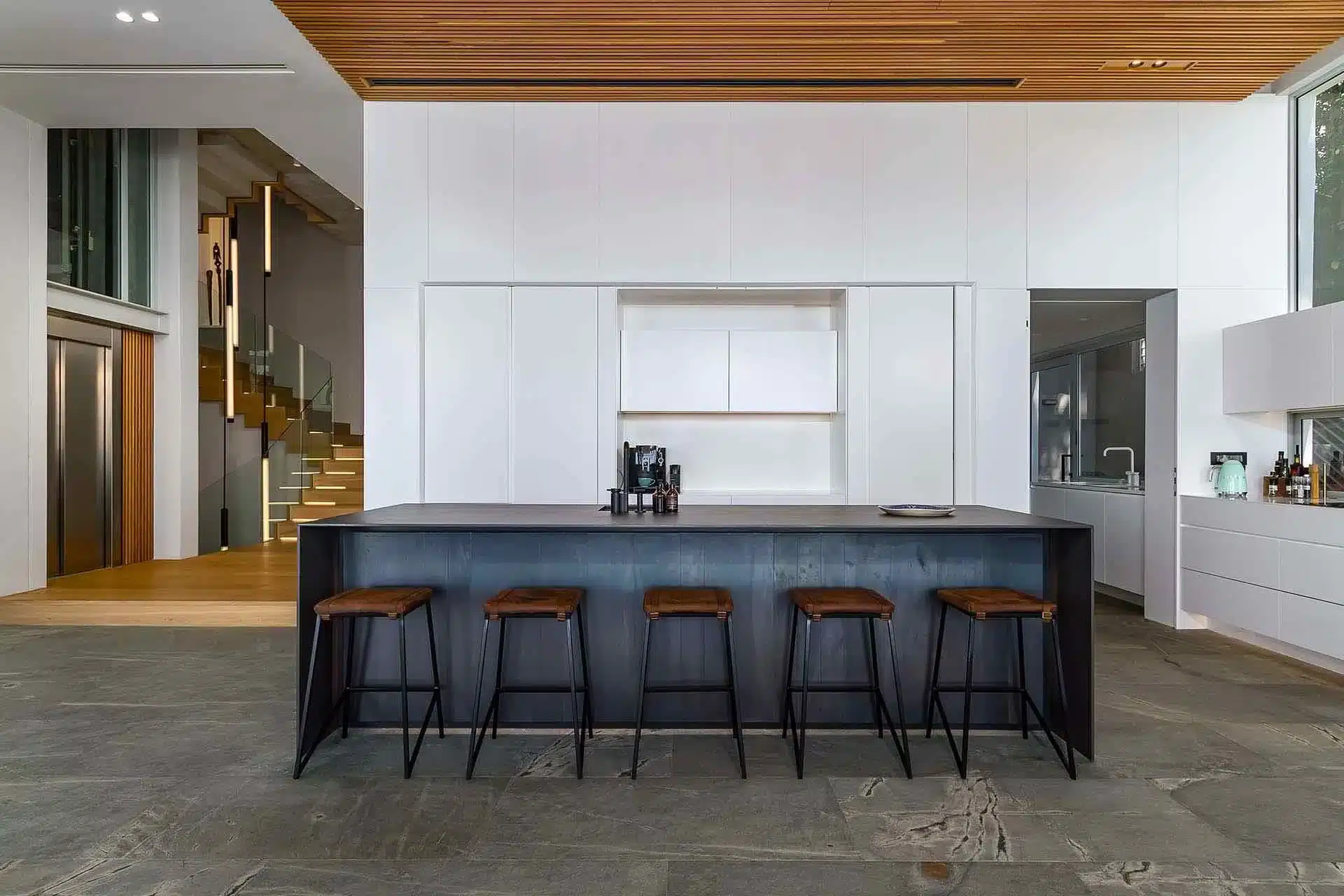 Modern kitchen with a large black island, five wooden stools, minimalist white cabinets—perfect for enjoying your luxury villa rental experience.