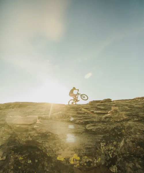 Mountain biker ascending rocky terrain at sunrise during the ABSA Cape Epic stage race in South Africa.